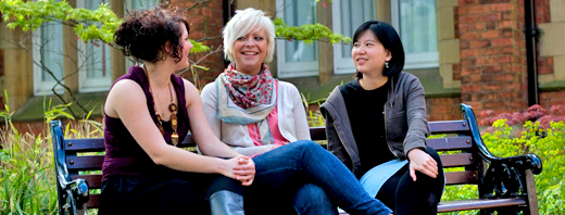 Three students sitting on a bench chatting
