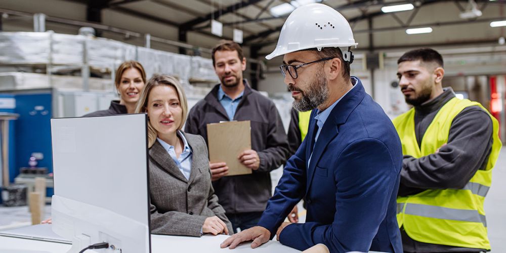 A team of engineers in an industrial setting consulting a computer screen.