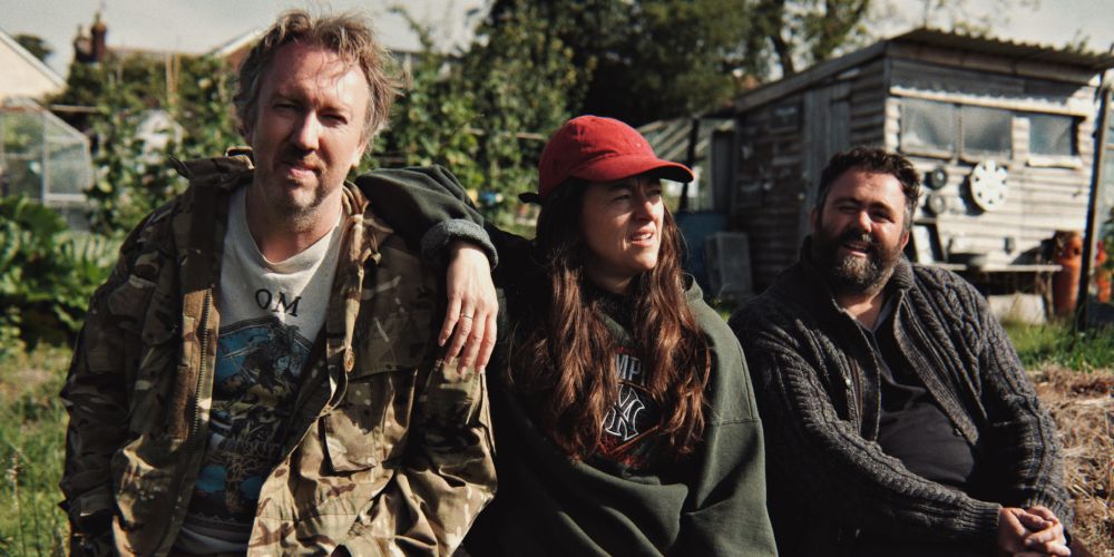 Three actors sit in a row on set