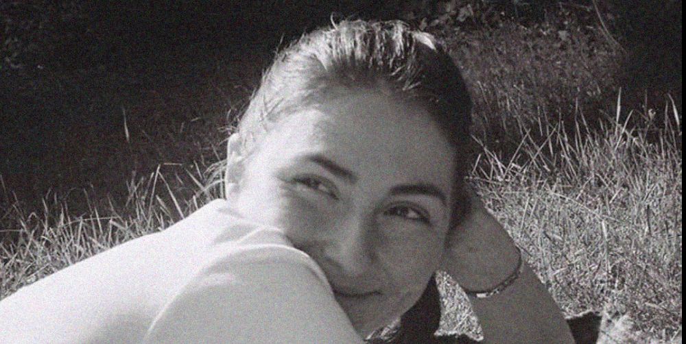 A black and white image of Anna May smiling, lying down, resting her head on her hand