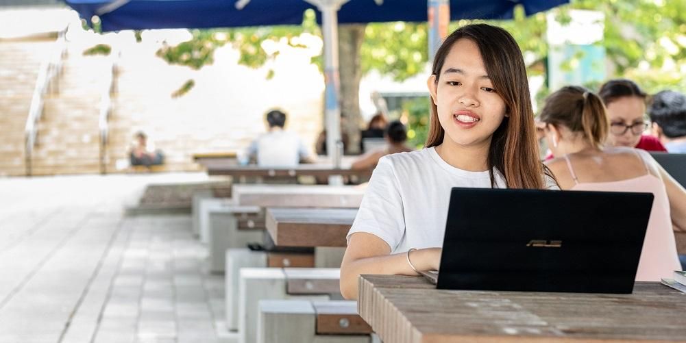 A student sat at a picnic bench using a laptop.