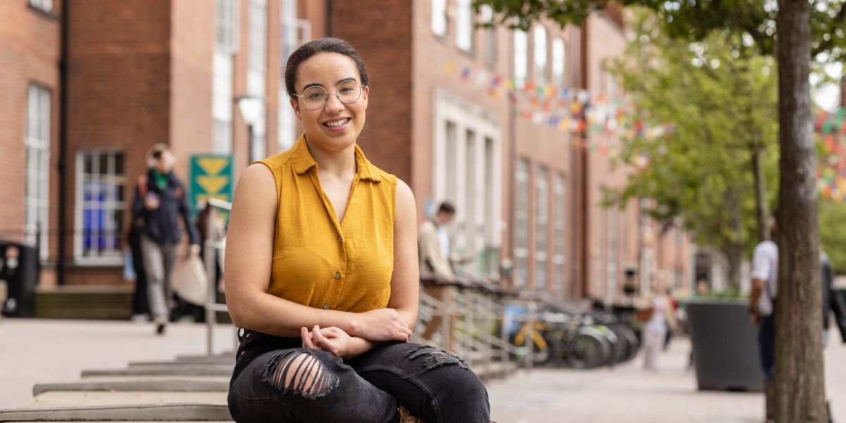 A student sat on a bench in front of the Leeds University Union, smiling.