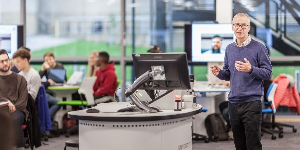 An academic speaking to a room of students sat at computers.