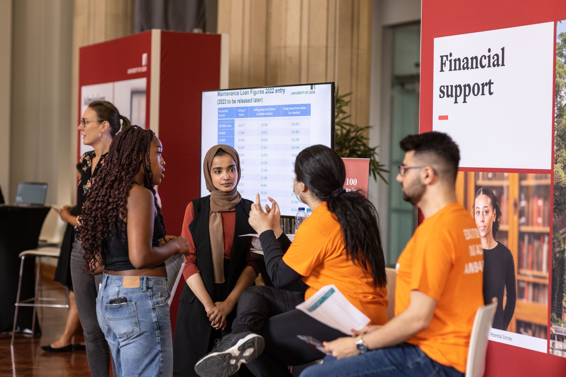 Two students talking to two ambassadors at the Open Day Information Fair. Behind them, a pull up banner says 'Financial support'.