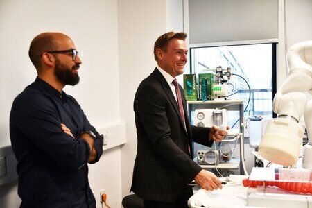 One man interacting with health technology machine and another man stood by his side watching.