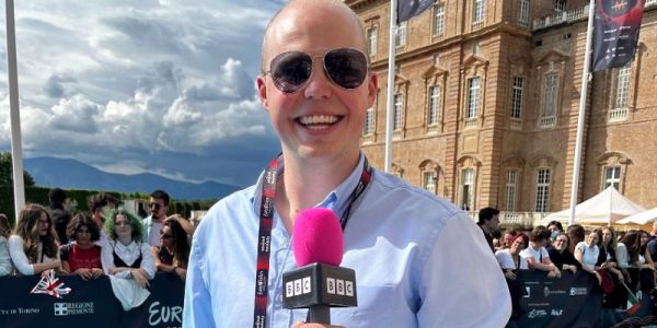 Joe Mason stands smiling with microphone ahead of broadcast