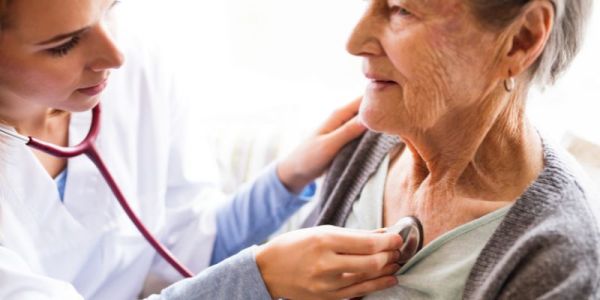 A doctor examines an older patient with a stethoscope to their chest