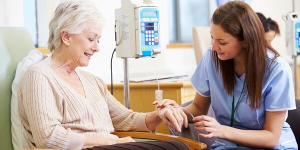 A nurse sitting next to a patient and administering chemotherapy via a tube into the patient&#039;s hand