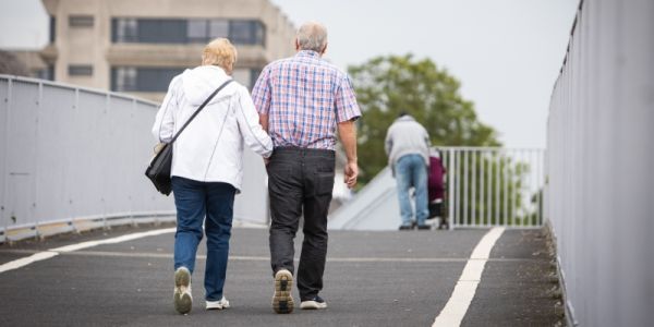 An older couple crossing a bridge arm in arm