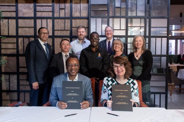 University of Leeds and University of Pretoria Vice Chancellors holding up signed agreement with a group of people standing up behind them.