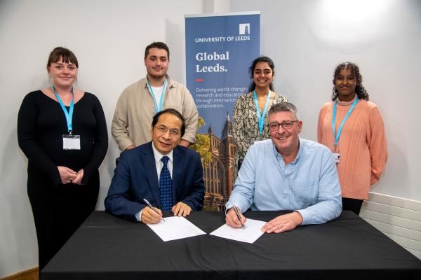 A group of four students stood behind two people signing the partnership agreement.