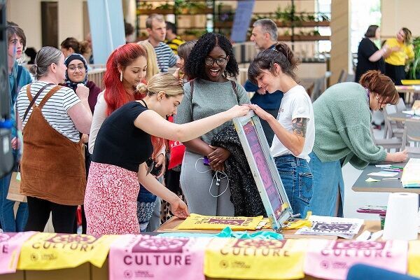 A group of people at an event. A few of them are watching someone create a screenprint