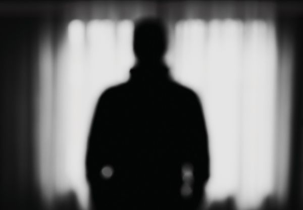 A silhouetted figure stands in front of a window