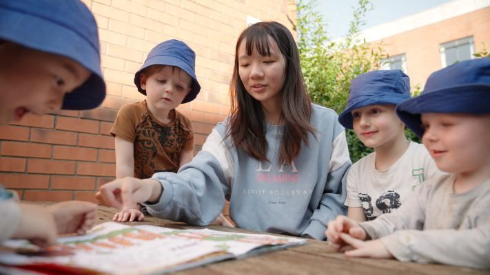 A group of four children reading a book with a University of Leeds student on placement at Bright Beginnings Nursery on campus.