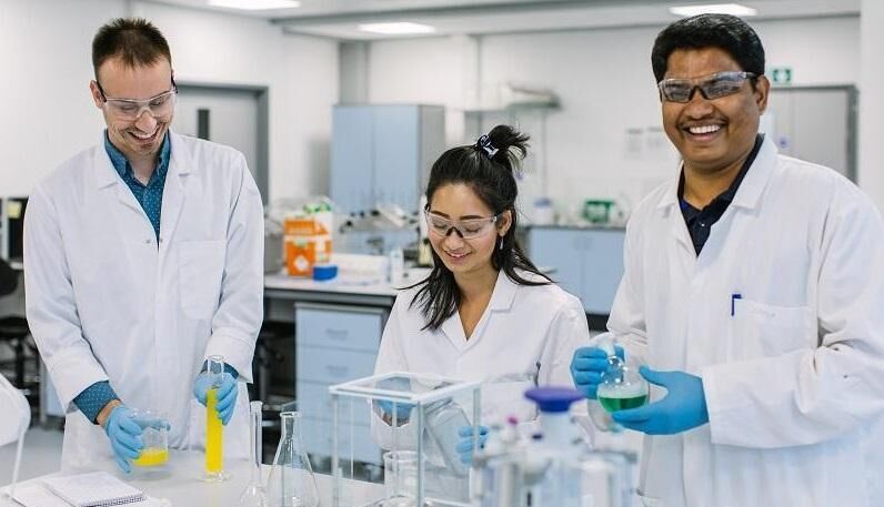 Three researchers in a lab wearing lab coats and holding test tubes and beakers.