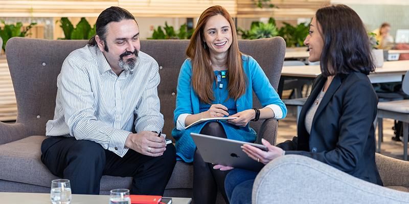 Three staff members sitting at a table having a conversation. One is holding a tablet