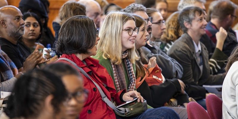 An audience of open day attendees sat down waiting for an event to start, chatting and smiling.