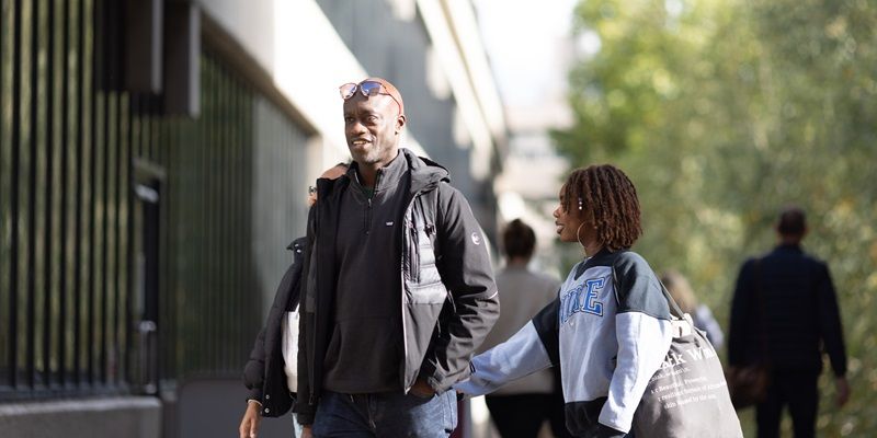 Two people walking around campus with a building and trees in the background