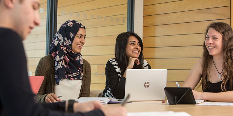 Four students sat around a table smiling and studying together.