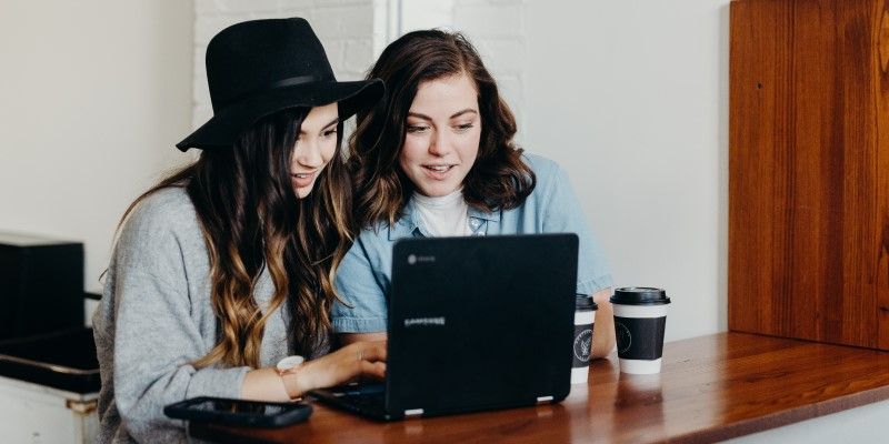 Two people looking at a laptop on a desk, with coffee cups next to it.