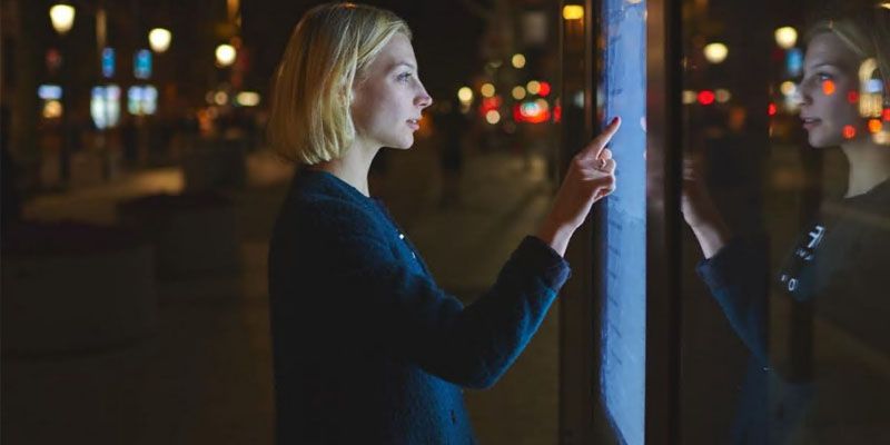A person interacting with a touch screen display on a street.