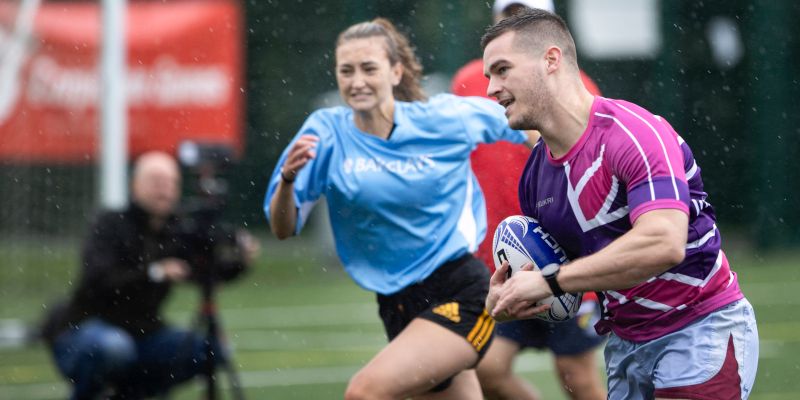 Two rugby players running on a field, one holding a rugby ball