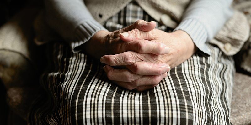 Sitting elderly woman with focus on her hands clasped on her lap