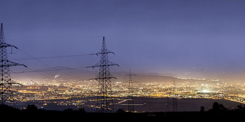 Electricity pylons in front of a brightly lit city at dusk.