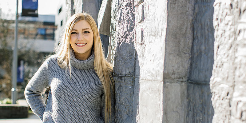 Smiling student leans against a wall outside on campus.