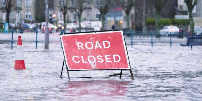 Road closed sign sitting in the middle of a flooded road.