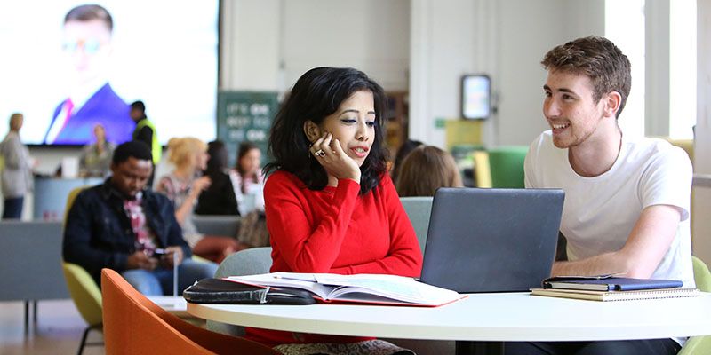 Two postgraduate students sat at a table looking at a laptop.