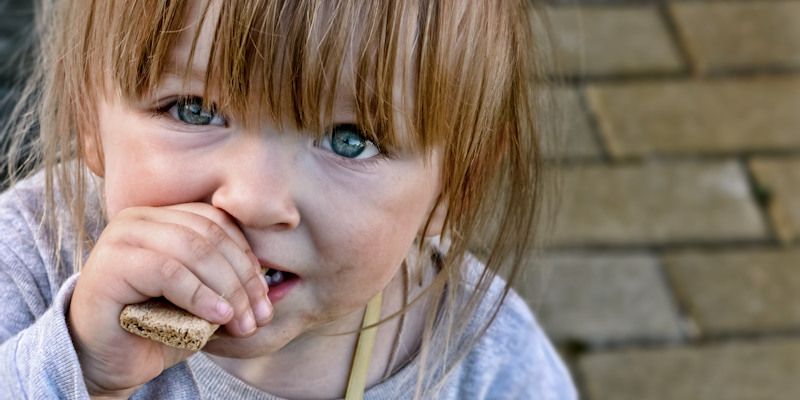 A small child looks up at the camera while eating a biscuit.