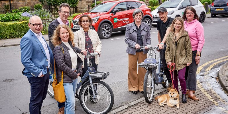 INFUZE partners pose with Beryl bikes by the side of the road. In the background are two Enterprise car club cars