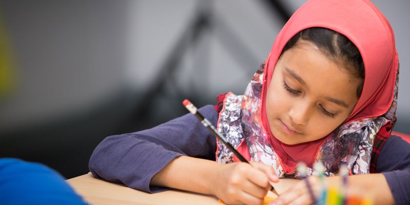 A young child sat at a table or desk using a pencil and paper