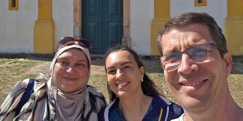 Three people stand facing the camera, smiling with the sun on their faces