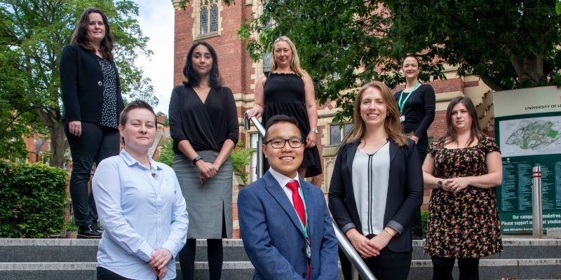 A group photo on the University of Leeds campus, with 8 fellows posing and smiling at camera