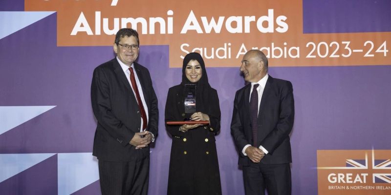 Manar stands on stage with her award, presented by two men either side of her