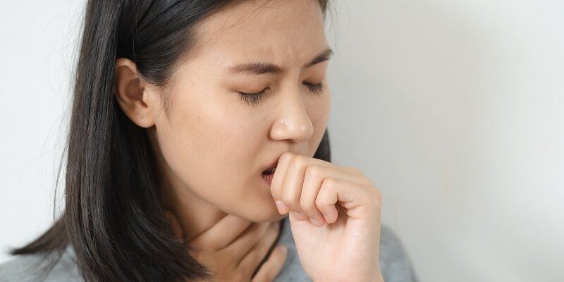 A woman has her hand in front of her mouth and by her throat as she appears to struggle with a dry mouth condition.