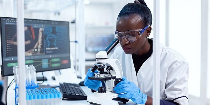 A scientist in the lab environment looking into a microscope.