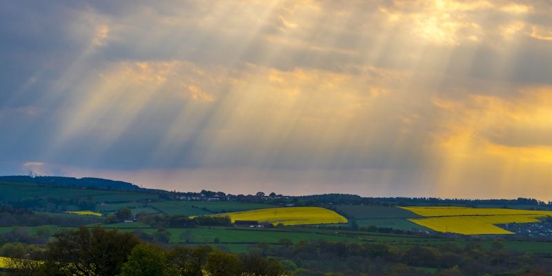 Sunlight breaking through storm clouds above a rural landscape.