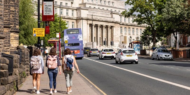 A group of three young people walking on the pavement alongside a road. The Parkinson Building is In the background