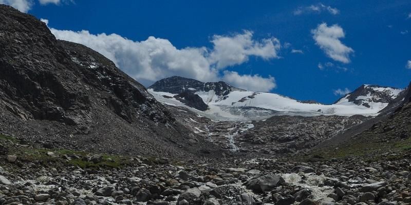 Odenwinkelkees glacier 
 with bare rocky mountainside on either side with bright blue sky in the background.