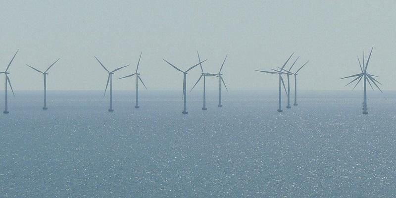 The images shows an offshore windfarm on a calm  day. The sea is flat.