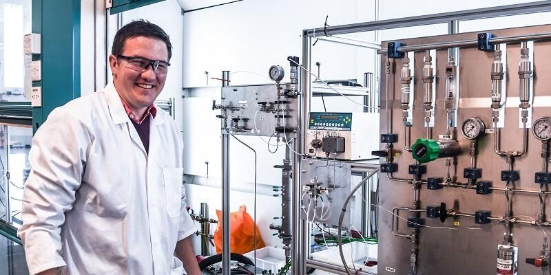 The picture shows Dr Rich Bourne standing by the side of a computer-driven chemistry platform. Dr Bourne is using robotocs and artificial intelligence to speed up the drug discovery process.