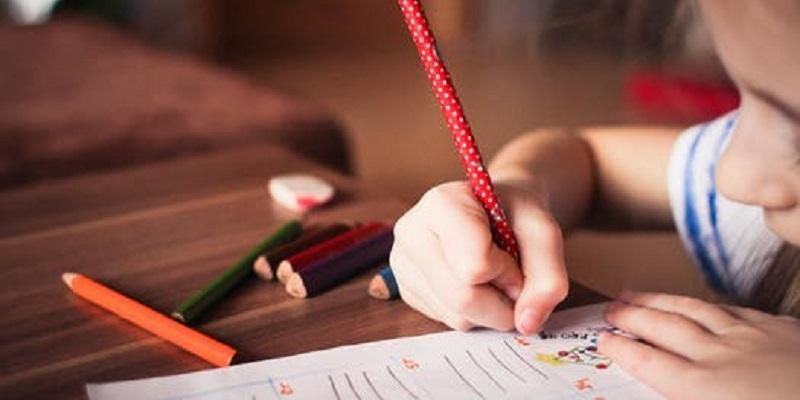 Child writing in a school text book. She has a pencil in her hand.