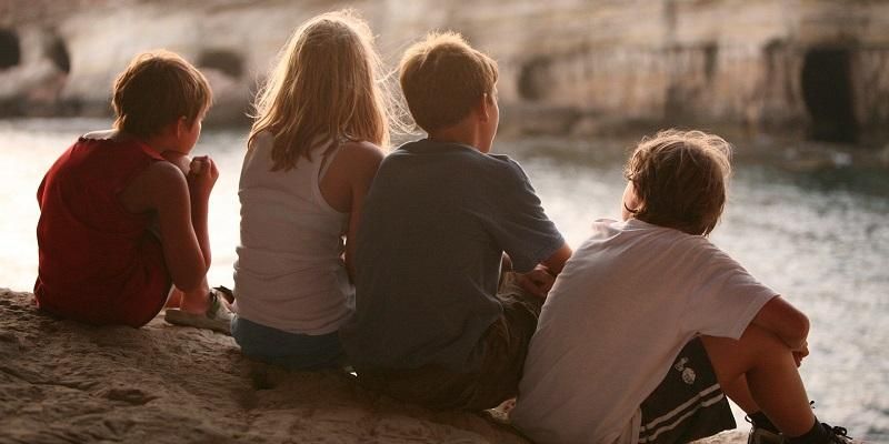 Four youngsters sitting by the side of a river chatting with their backs to the camera.