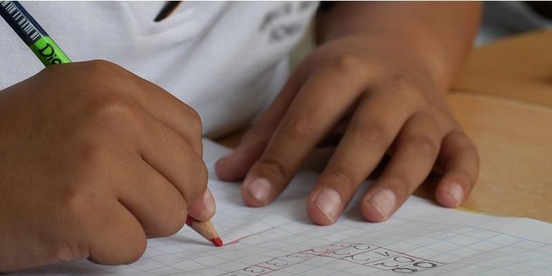 Picture shows a young child writing in his school maths book