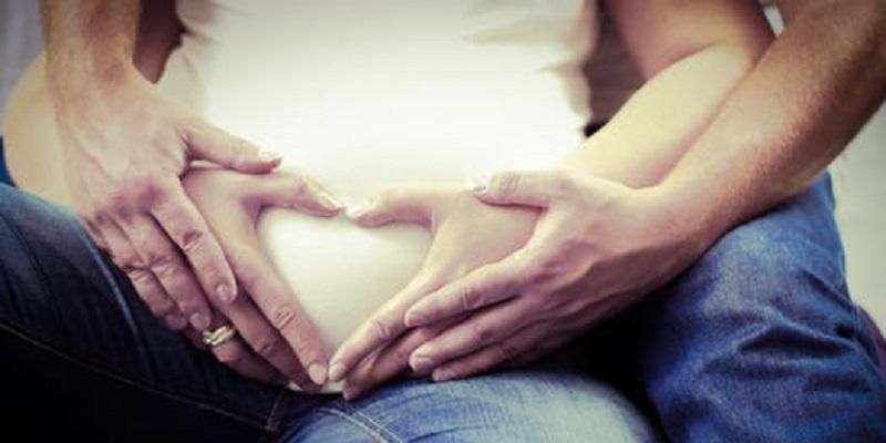 Image shows a woman holding hands with a pregnant bumb