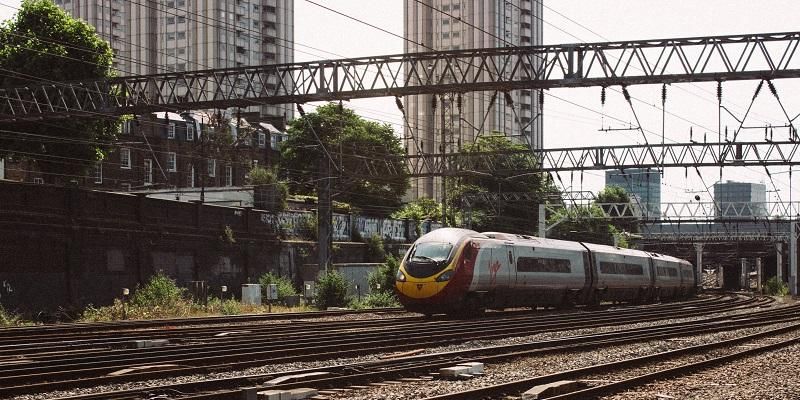 The picture shows a train going through a busy rail junction. There are overhead power lines.