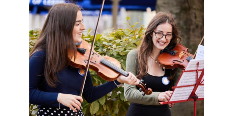 Two women smiling looking at sheet music and playing violins